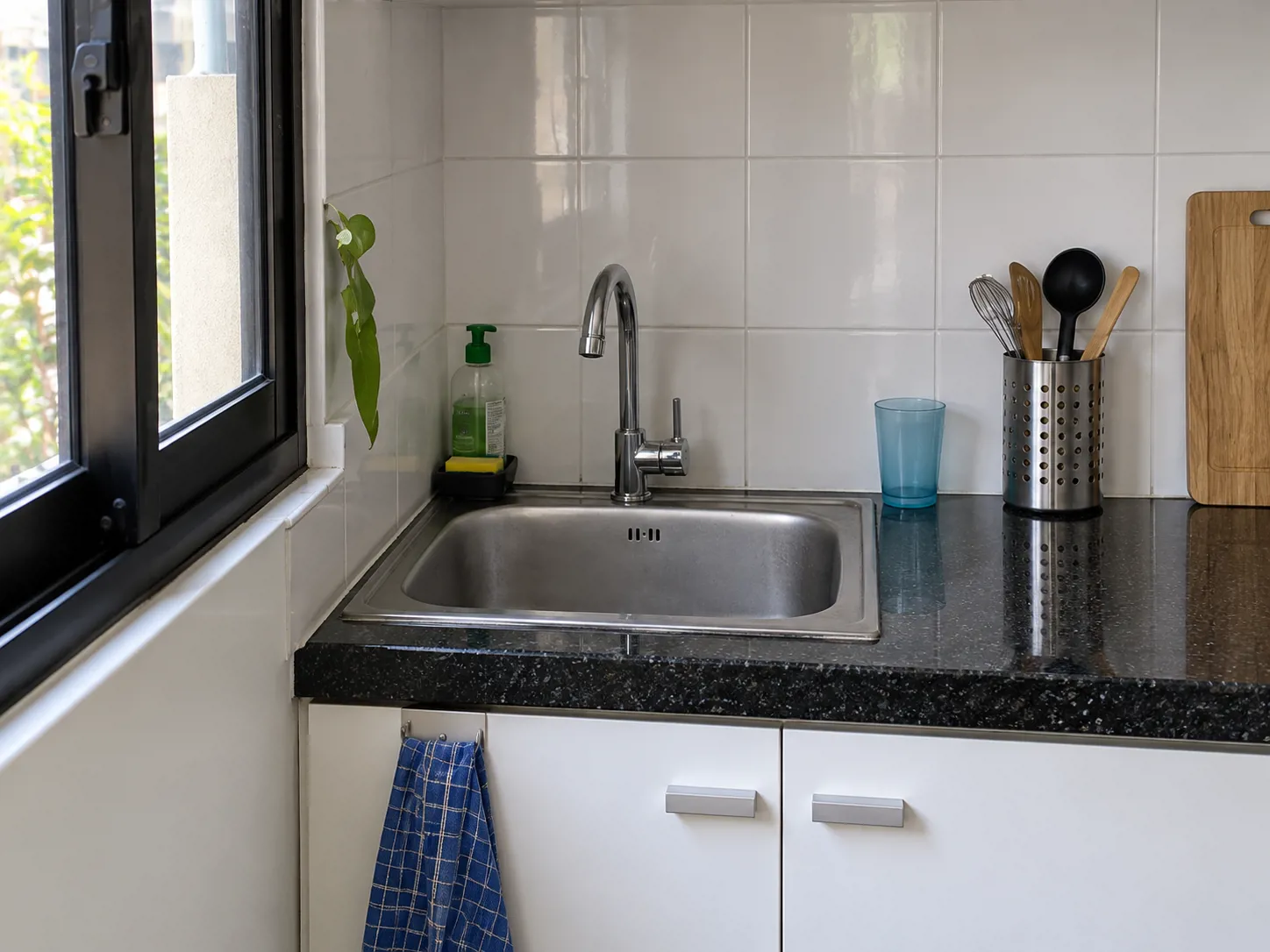 Sink topmount stainless dan granit hitam menata area cuci di ujung meja, menyisakan bidang tengah untuk menyiapkan bahan.